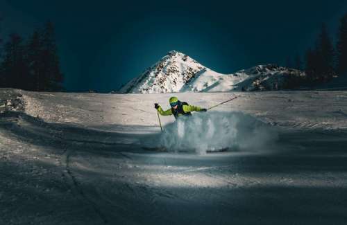skieur dérapant en envoyant de la neige devant une montagne